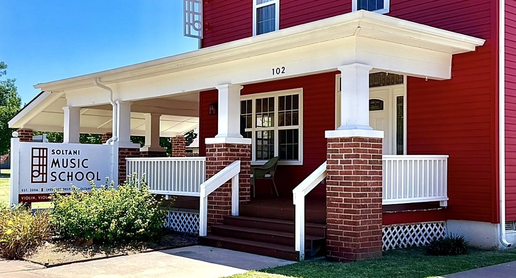 The wrap-around front porch of Soltani Music School: brick piers, tapered white columns, red siding